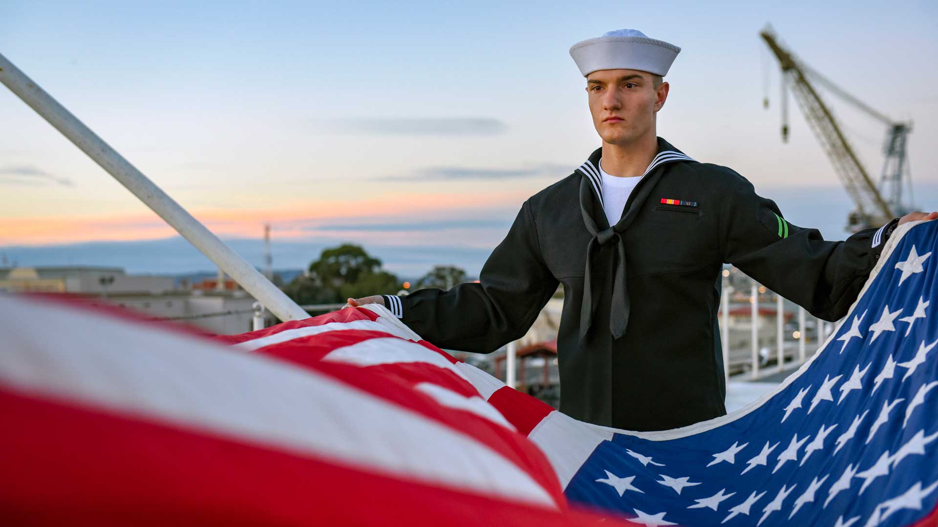A Navy Sailor helps fold the United States flag during an evening colors ceremony aboard a Navy ship.