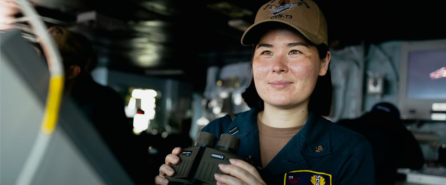 A United States Navy Judge Advocate General (JAG) officer holds binoculars on the bridge of the USS George Washington.
