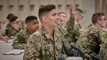 A student in a U.S. Navy classroom raises his hand to answer a question.