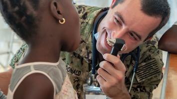 Navy physician smiling while examining a young girl's ear with an otoscope during a humanitarian mission in Haiti.